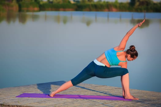 girl doing yoga exercises on the river bank at sunset