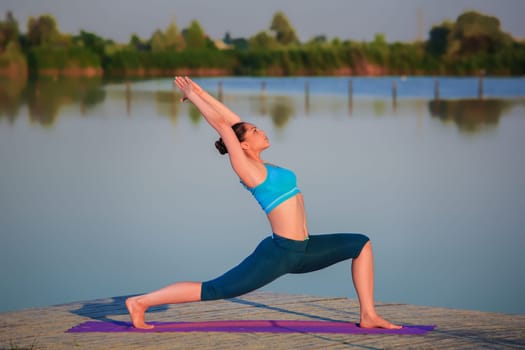 girl doing yoga exercises on the river bank at sunset