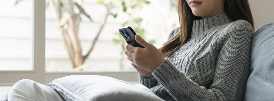 Young asian woman using mobile phone. Social media messaging Woman sitting on sofa playing with phone.