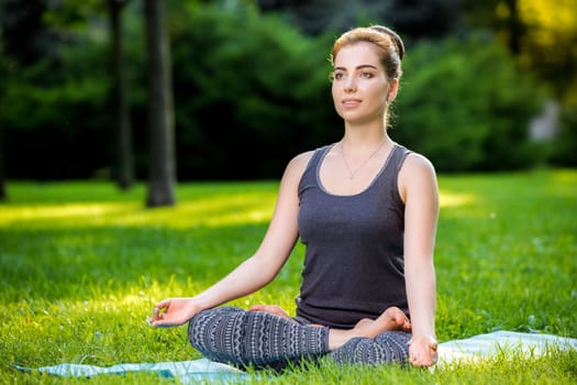 Meditating woman in meditation in city park in yoga pose. Girl relaxing with serene relaxed expression outside in summer. Beautiful young Caucasian female model.