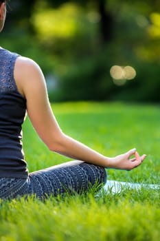 Meditating woman in meditation in city park in yoga pose. Girl relaxing with serene relaxed expression outside in summer. Beautiful young Caucasian female model. Close up
