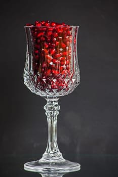 Still live of a single cut crystal glass filled with shiny pomegranitate seeds.