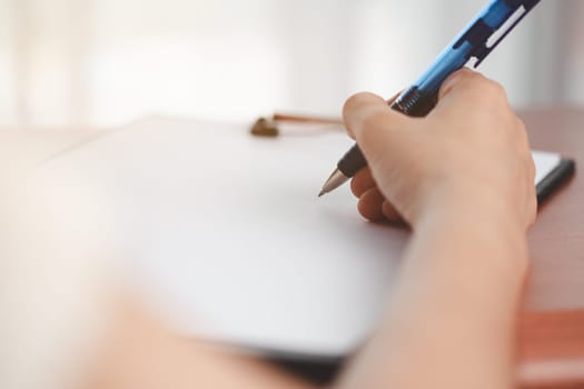 Asian woman's hand holding a pen and writing something on the notebook for the concept of work and study.