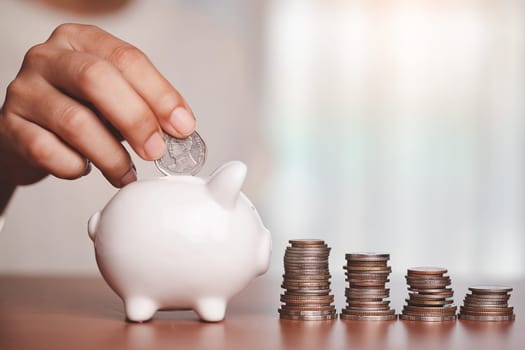 Asian women's hand saving a coin into piggy bank with step of coins and money on the wooden table for investment, business, finance and saving money concept.