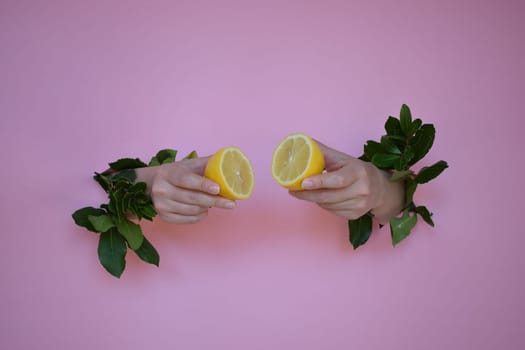 Two pieces of lemon in the hands of a girl, on a pink background.