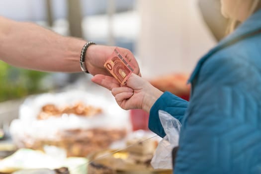 Buy sweets in a confectionery shop. The woman takes a bag of sweet biscuits from the seller and pays him. Hands of the seller and the buyer with money close-up. Copy space