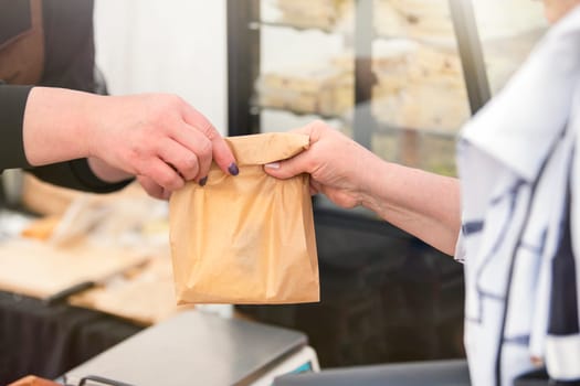 Buy sweets in a confectionery shop. The woman takes a bag of sweet biscuits from the seller and pays him. Hands of the seller and the buyer with money close-up. Copy space