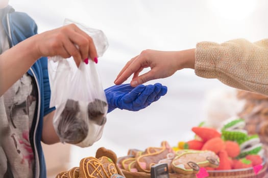 Buy sweets in a confectionery shop. The woman takes a bag of sweet biscuits from the seller and pays him. Hands of the seller and the buyer with money close-up. Copy space