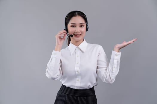 Asian female call center operator with smile face advertises job opportunity, wearing a formal suit and headset holding hand gesture for product on customizable isolated background. Enthusiastic