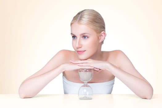 Personable model holding hourglass in beauty concept of anti-aging skincare treatment for woman. Young girl portrait with perfect smooth clean skin and flawless soft makeup in isolated background.