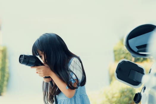 A playful girl holding and pointing an EV plug, a home charging station providing a sustainable power source for electric vehicles. Concept of progressive new generation with ecological awareness.