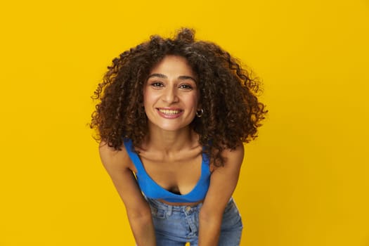 Woman with curly afro hair in a blue t-shirt on. yellow background signs with her hands, look into the camera, smile with teeth and happiness, copy space. High quality photo