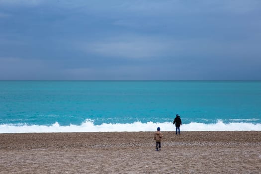 Two boys watching the waves. Storm in the Mediterranean Sea. Beautiful rocky shore with rolling waves. Turkiye, Antalya.