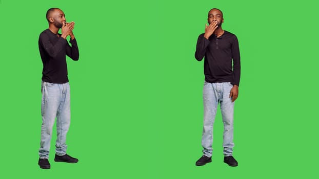 African american man sending air kisses on camera, posing with kissy face on full body greenscreen. Young adult being romantic in studio and doing flirty gesture, optimistic reaction.