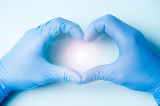 The hands of a doctor in blue gloves show the heart on a light background, as a symbol of medicine taking care of the patient's health.
