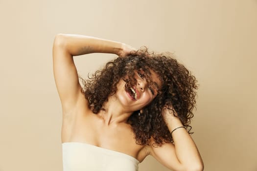 Woman applies cream and balm to her curly hair, the concept of protection and care, a healthy look, a smile with teeth on a beige background.