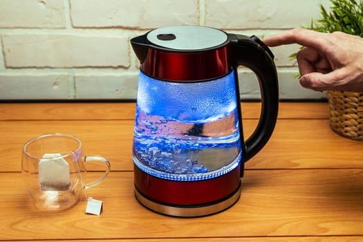 morning or evening tea drinking. a man turns off the heating button of a modern glass electric kettle on the background of a brick wall