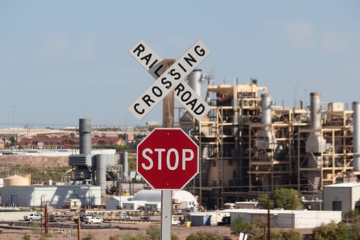 Railroad crossing sign on blue sky and with active factory in the back.