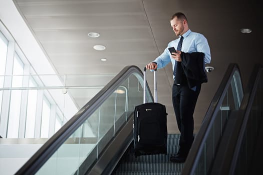 Travel is all part of the job. a businessman traveling down an escalator in an airport