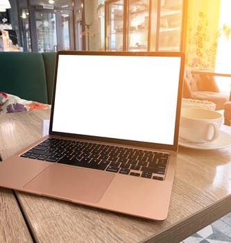 Mock up of generic laptop computer with blank copy space screen for your text or advertising content. Workspace of young freelancer: open notebook pc, cell phone and cappuccino on table in the cafe