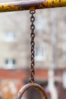 An iron chain with gray and translucent oval rings on a gray background in the courtyard of a multi-storey building. A place of rest and activities for children