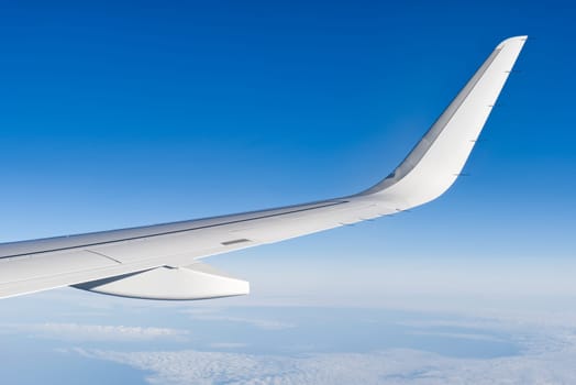 Airplain wing view thrue window in the sky. Clouds and sky as seen through porthole of an aircraft with airplane's wing