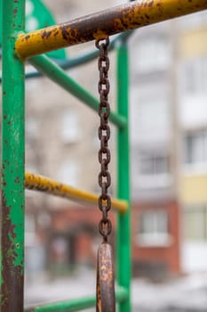 An iron chain with gray and translucent oval rings on a gray background in the courtyard of a multi-storey building. A place of rest and activities for children