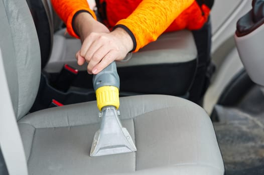 Handyman vacuuming car front textile seat with vacuum cleaner. man cleaning work Minivan.