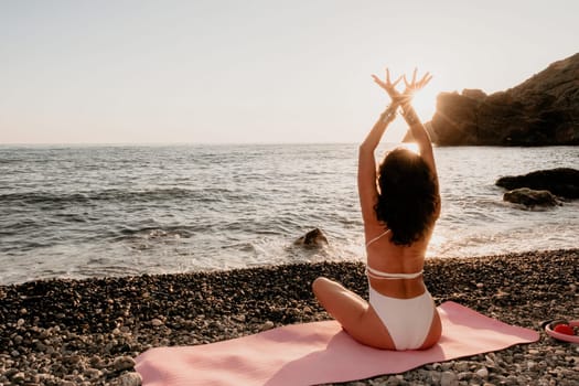 Young woman in swimsuit with long hair practicing stretching outdoors on yoga mat by the sea on a sunny day. Women's yoga fitness pilates routine. Healthy lifestyle, harmony and meditation concept.