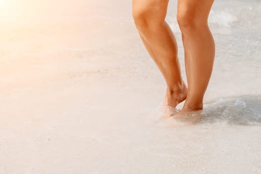 Sea beach travel - woman walking on sand beach leaving footprints in the white sand. Female legs walking along the seaside barefoot, close-up of the tanned legs of a girl coming out of the water