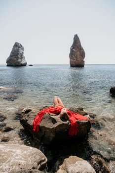 Woman travel sea. Young Happy woman in a long red dress posing on a beach near the sea on background of volcanic rocks, like in Iceland, sharing travel adventure journey