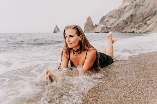 Woman travel sea. Young Happy woman in a long red dress posing on a beach near the sea on background of volcanic rocks, like in Iceland, sharing travel adventure journey