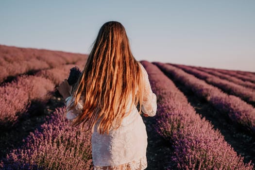 Close up portrait of young beautiful woman in a white dress and a hat is walking in the lavender field and smelling lavender bouquet.