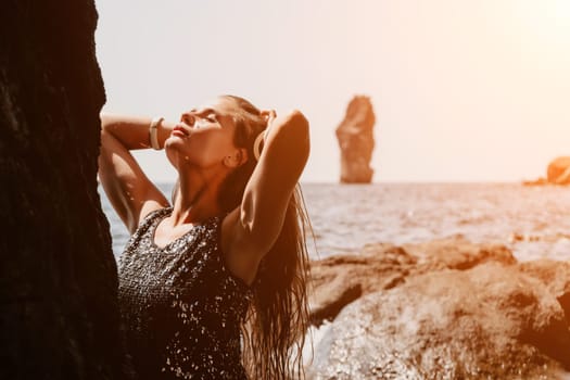 Woman travel sea. Young Happy woman in a long red dress posing on a beach near the sea on background of volcanic rocks, like in Iceland, sharing travel adventure journey