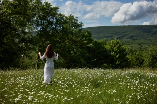 a woman in a light dress stands far away in a field of daisies with her back to the camera raising her hands to the sky. High quality photo