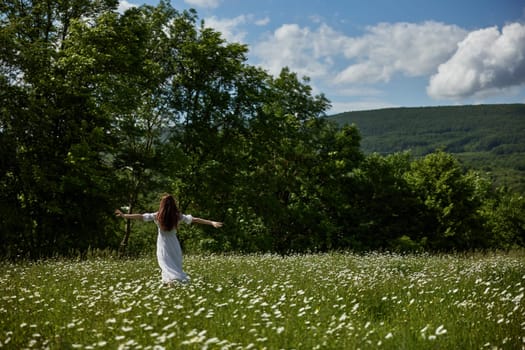 a woman in a light dress stands far away in a field of daisies with her back to the camera raising her hands to the sky. High quality photo