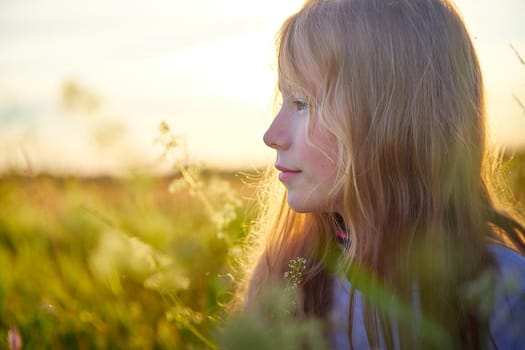 Portrait of pretty blonde girl having fun in a meadow on a natural landscape with grass and flowers on a sunny summer day. Portrait of a teenage child in summer or spring outdoors on field