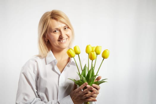 Beauty young blonde happy woman with bouquet of yellow tulips on white background. The concept of holiday and a gift for a lady and a girl. . Copy space