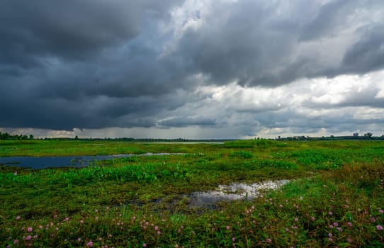 Landscape of green grass field and overcast sky. Dark cloudscape of a stormy sky. Natural water reservoir. Water sustainability. Freshwater for human consumption. Sustainable sources of water.
