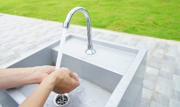 World water day concept. Woman washing hands with tap water under faucet at white sink. Washing hands with tap water at outdoor sink near green grass lawn. Personal hygiene. Water consumption.                         