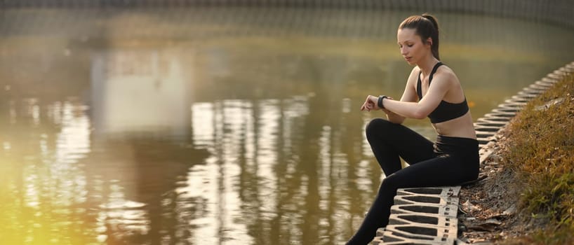 Beautiful sporty woman counting calories burned or checking fitness results on smartwatch after workout session.