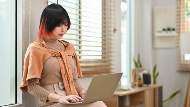 Young stylish woman using laptop at home office. Freelance, creative occupation, e-learning concept.