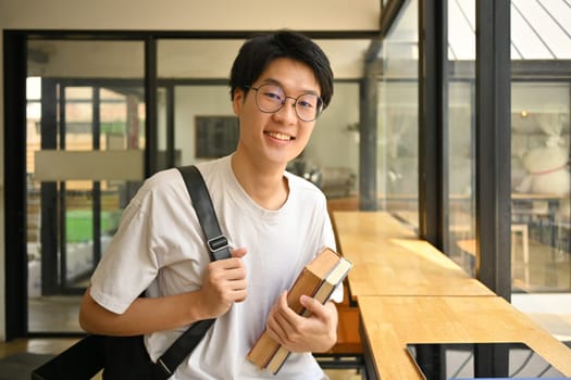 Asian male university student in glasses holding books and smiling to camera. Education, school, college concept.
