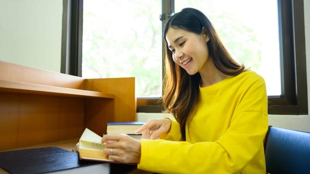 Peaceful woman reading interesting book, preparing for exam in library. People, knowledge and education concept.