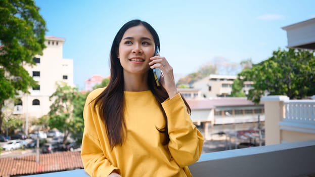 Stylish young woman talking to friends on mobile phone while standing on the balcony of a modern office.