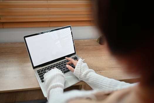 Over shoulder view of young woman hands typing on laptop keyboard. Empty screen for your advertising text message.