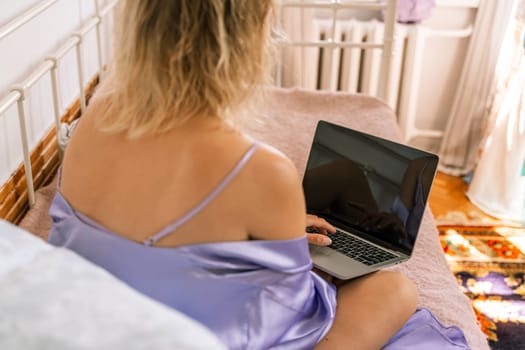 A top view of a woman in a purple nightgown using a laptop on a bed, suggesting that she is working or studying from the comfort of her own home