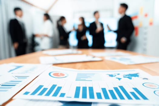 Closeup focus on financial report foreground, performance result paper with blur background of office workers, colleagues interacting, working together in harmony office meeting room.