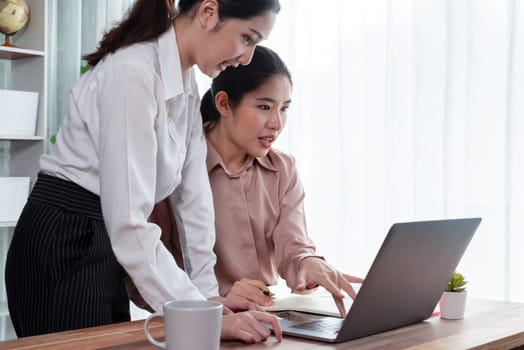 Two young office lady colleagues collaborating in modern office workspace, engaging in discussion and working together on laptop, showcasing their professionalism as modern office worker. Enthusiastic