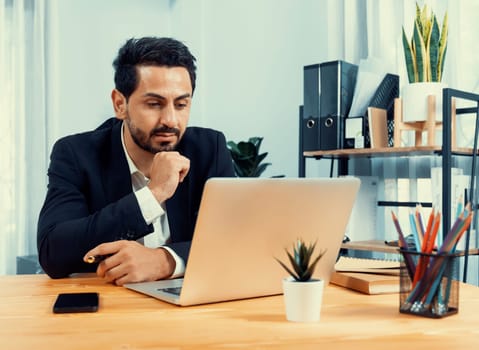 Modern professional businessman at modern office desk using laptop to work and write notes. Diligent office worker working on computer notebook in his office work space. fervent